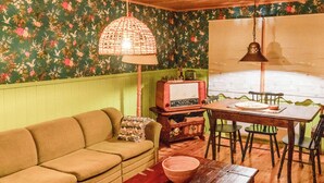 Una habitación acogedora con papel tapiz floral verde, un sofá marrón, una mesa de madera con sillas y una radio antigua.