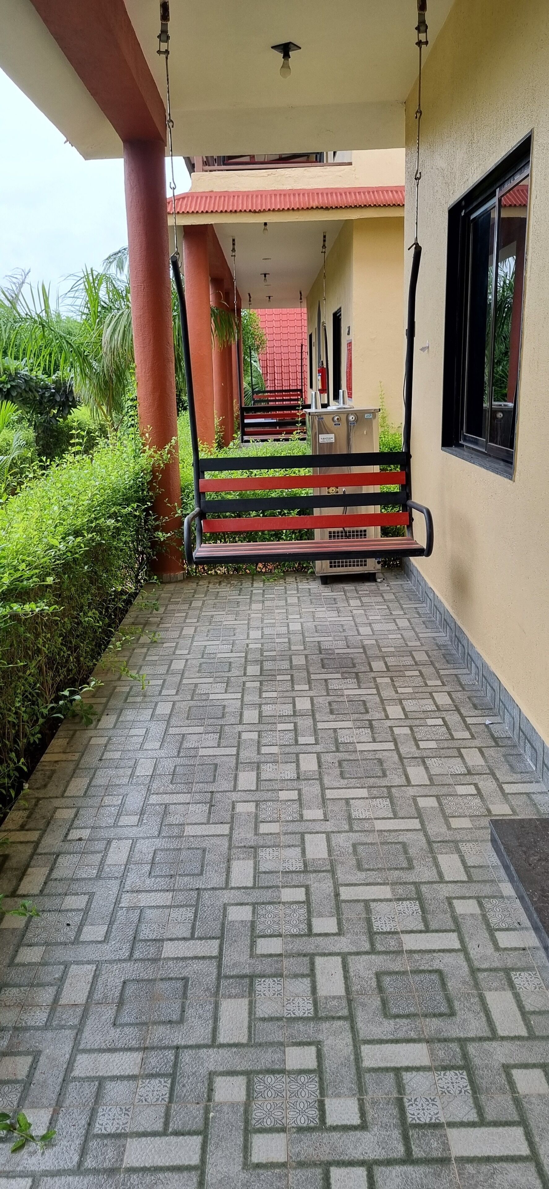 A covered walkway with a patterned tile floor, a bench, and a building with a red roof in the background.