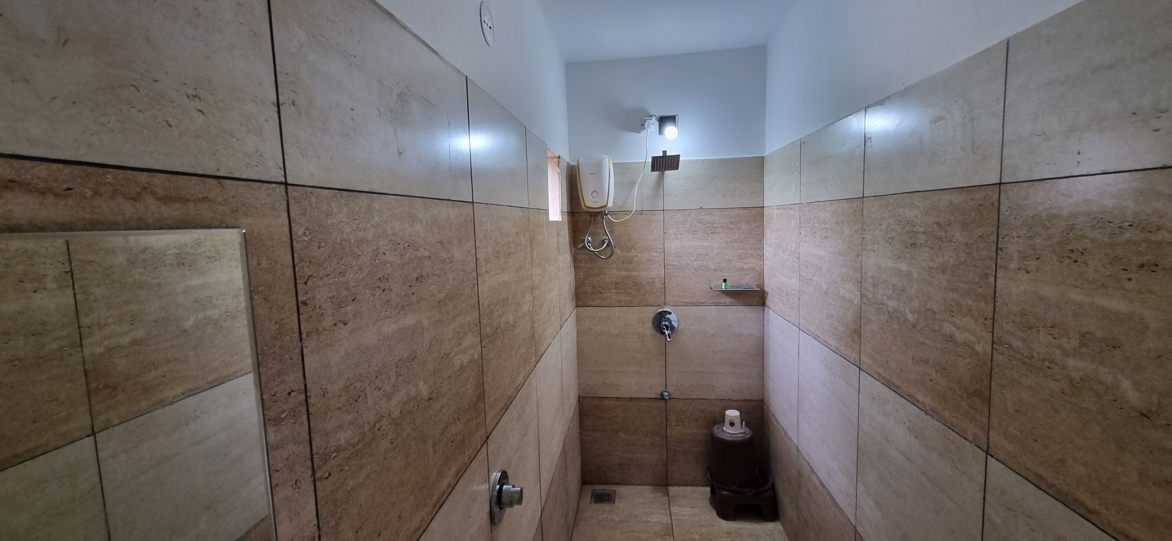 Une petite salle de bain carrelée, équipée d’une douche, d’un sèche-mains et d’un porte-rouleau de papier toilette.