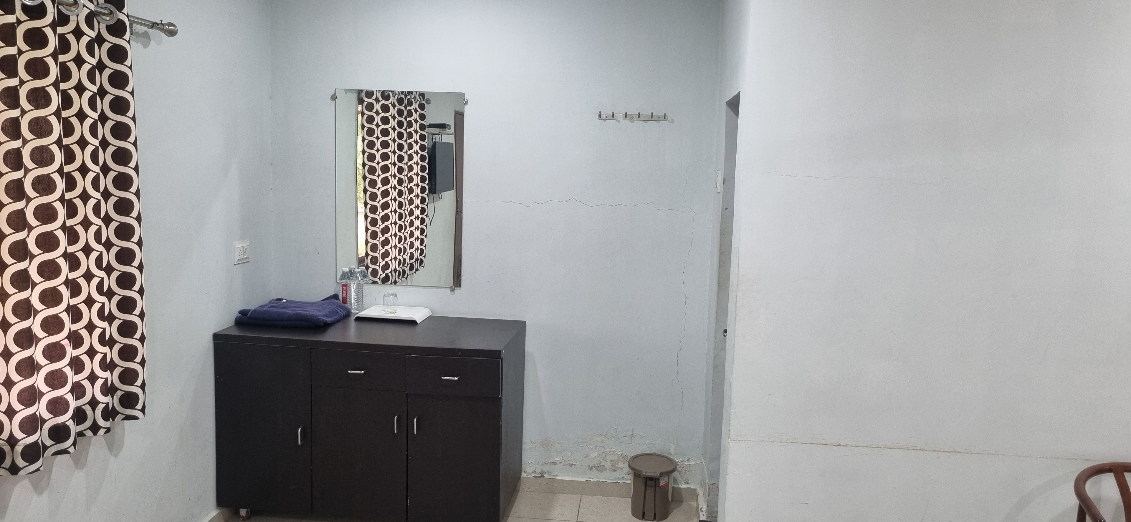 A bathroom with a dark wooden cabinet, a mirror, and a patterned curtain.