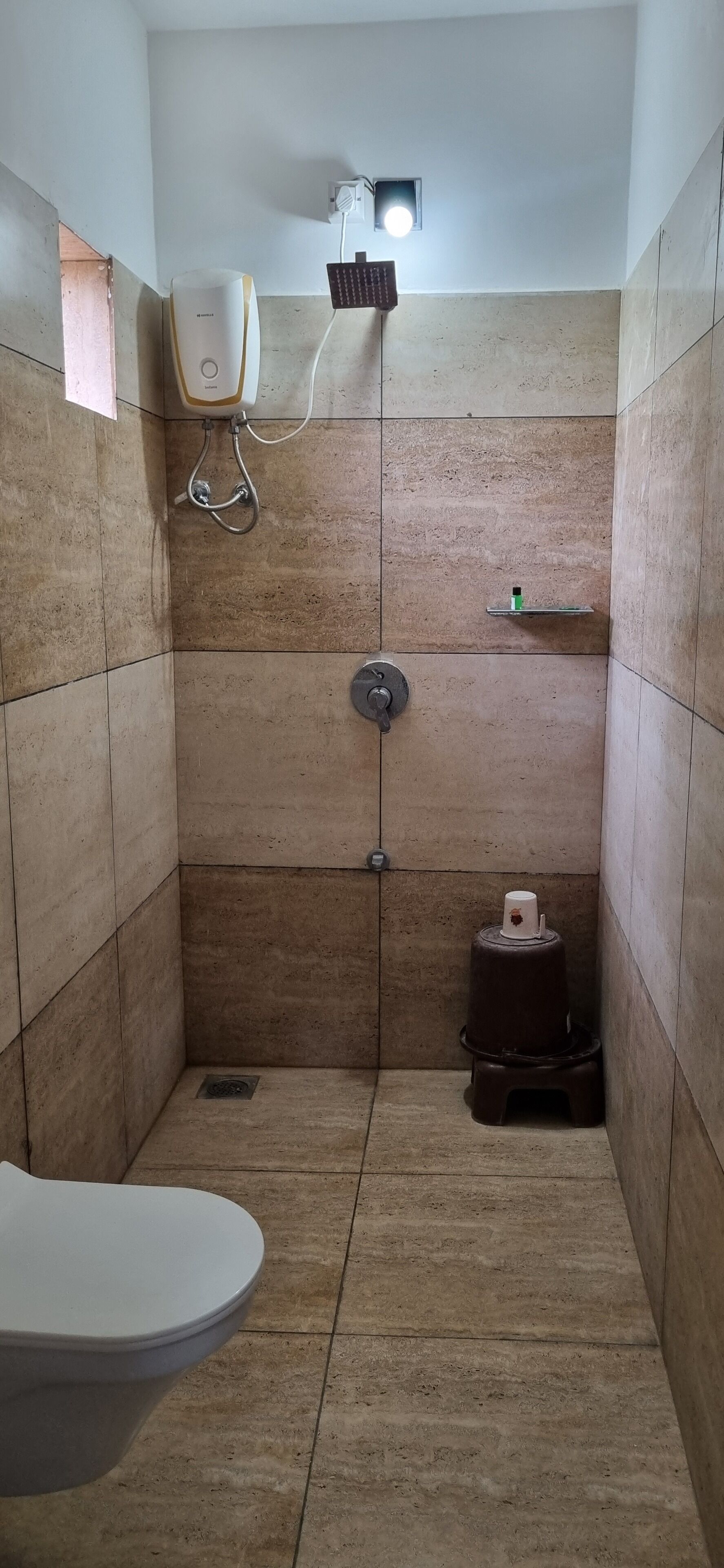 Une petite salle de bain carrelée, équipée de toilettes, d’une douche et d’une cuisinière à gaz.