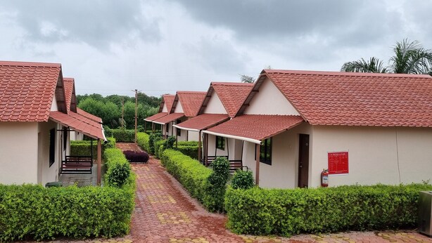A row of bungalow-style buildings with red-tiled roofs and a paved pathway leading through neatly trimmed hedges. - PATANG FAMILY RESORT (Talala)