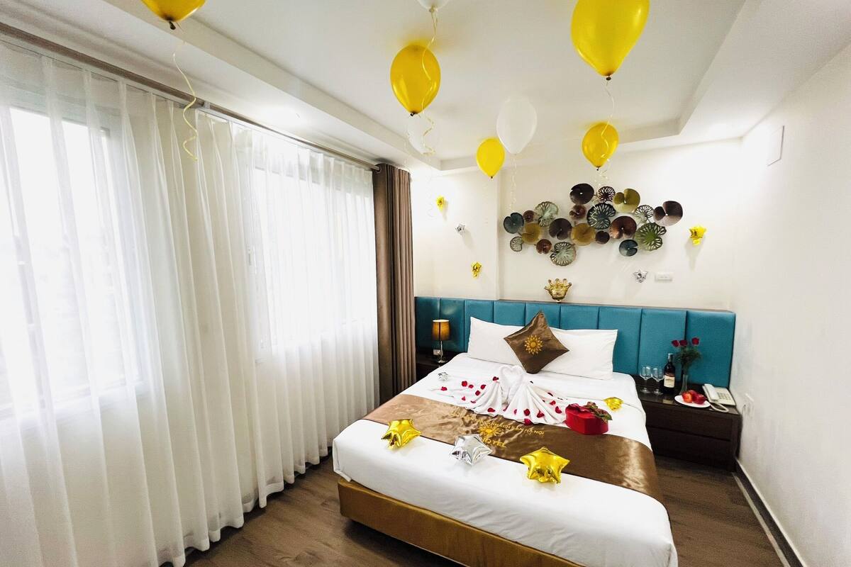 A hotel room with a bed, curtains, a nightstand, a wall with decorative plates, and balloons.