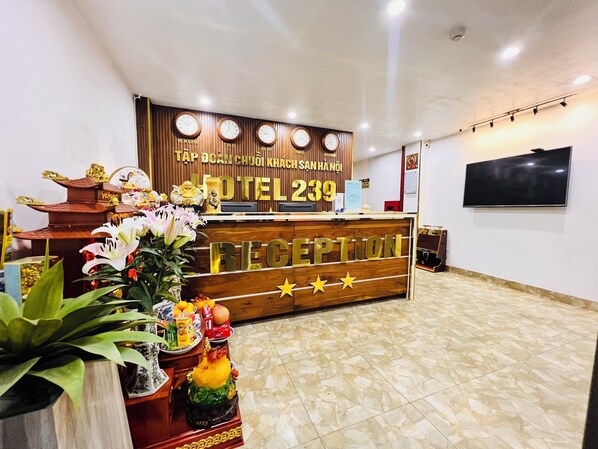 A hotel reception desk with a wooden finish, a clock above it, and a TV mounted on the wall. - 239 Hotel (Hanoi)