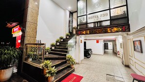 Entrada de un hotel con una escalera que conduce al piso superior, un tapete de bienvenida rojo y un letrero que indica el número 239 del hotel.
