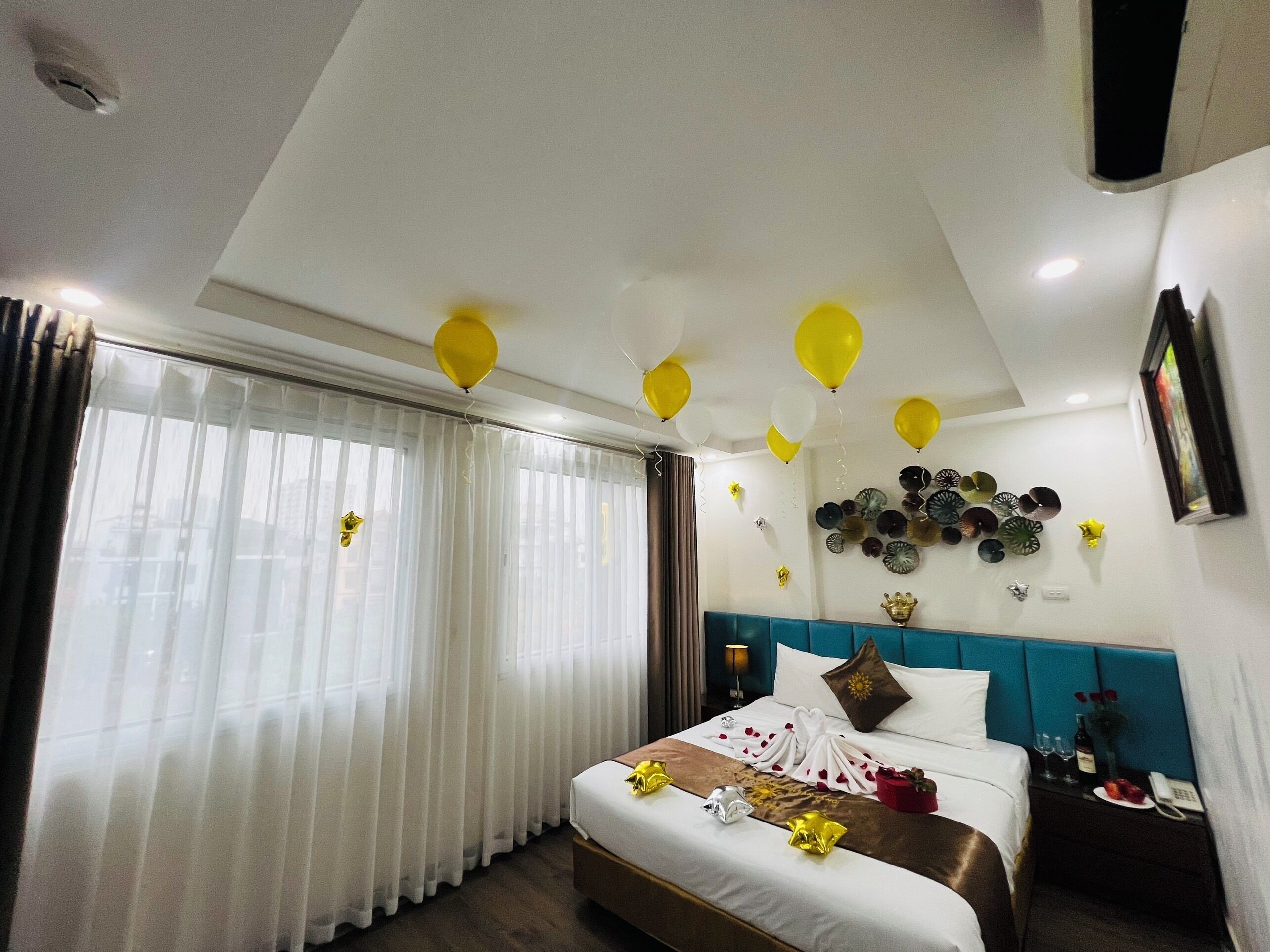 A hotel room with a bed, curtains, a wall with decorative plates, and balloons.