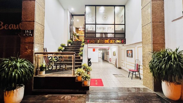 Entrada de hotel con una escalera que lleva al segundo piso, plantas en macetas y un felpudo.