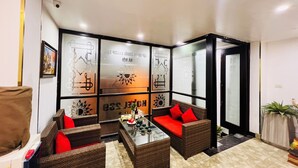 Un hall con muebles de mimbre, una mesa de centro de vidrio y paneles decorativos en la pared.