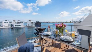 Une table à manger avec des assiettes, des verres et un barbecue, installée sur une terrasse donnant sur une marina.