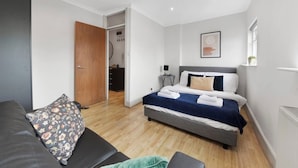 A modern bedroom with a bed, a sofa, a wooden door, and a small desk. - Crouch Hill N4, Crouch Hill, Finsbury Park (London)
