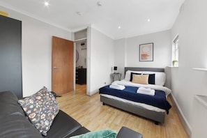 A modern bedroom with a bed, a sofa, a wooden door, and a small desk.