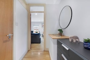 A hallway leading to a living area with a sofa, a small table with decorative items, and a wall-mounted mirror.