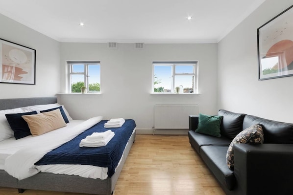 A modern bedroom with a bed, a sofa, two windows, and a radiator.