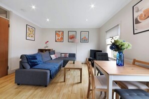 A modern living room with a grey sofa, a wooden dining table, and a TV.