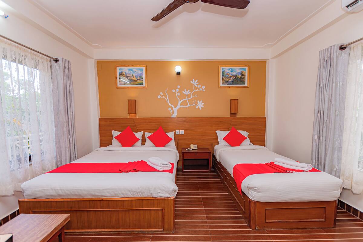 A hotel room with two beds, a wooden headboard, a small bedside table with a phone, and a wall-mounted light.