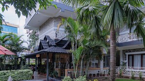 An outdoor dining area with a table set for four, surrounded by palm trees and a building with a balcony. - Basundhara Resort Pokhara (Pokhara)