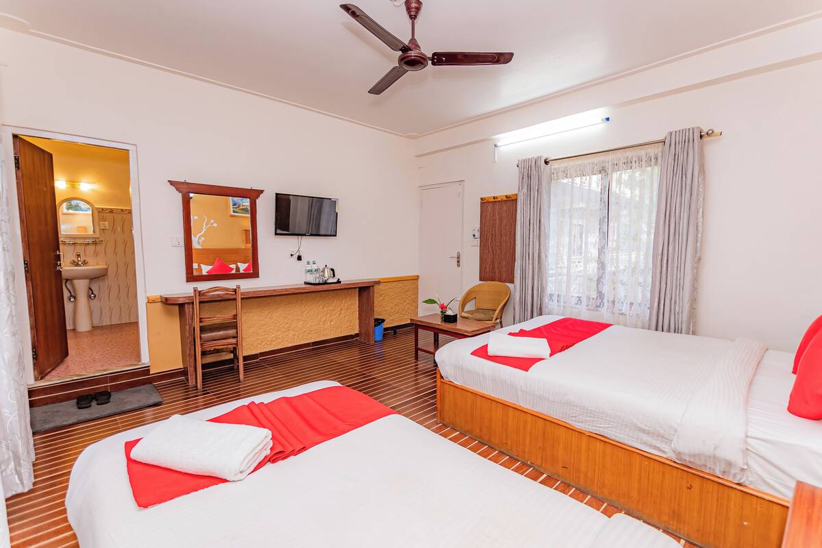 A hotel room with two beds, a desk, a chair, a television, and a ceiling fan.