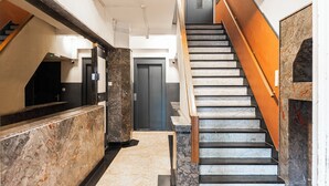 Un moderno vestíbulo de hotel con un mostrador de recepción de mármol, una escalera con barandillas de madera y una puerta oscura al final.