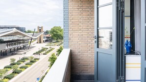 Un balcón con vista a un edificio moderno, un muro de ladrillo y una puerta con ventana.