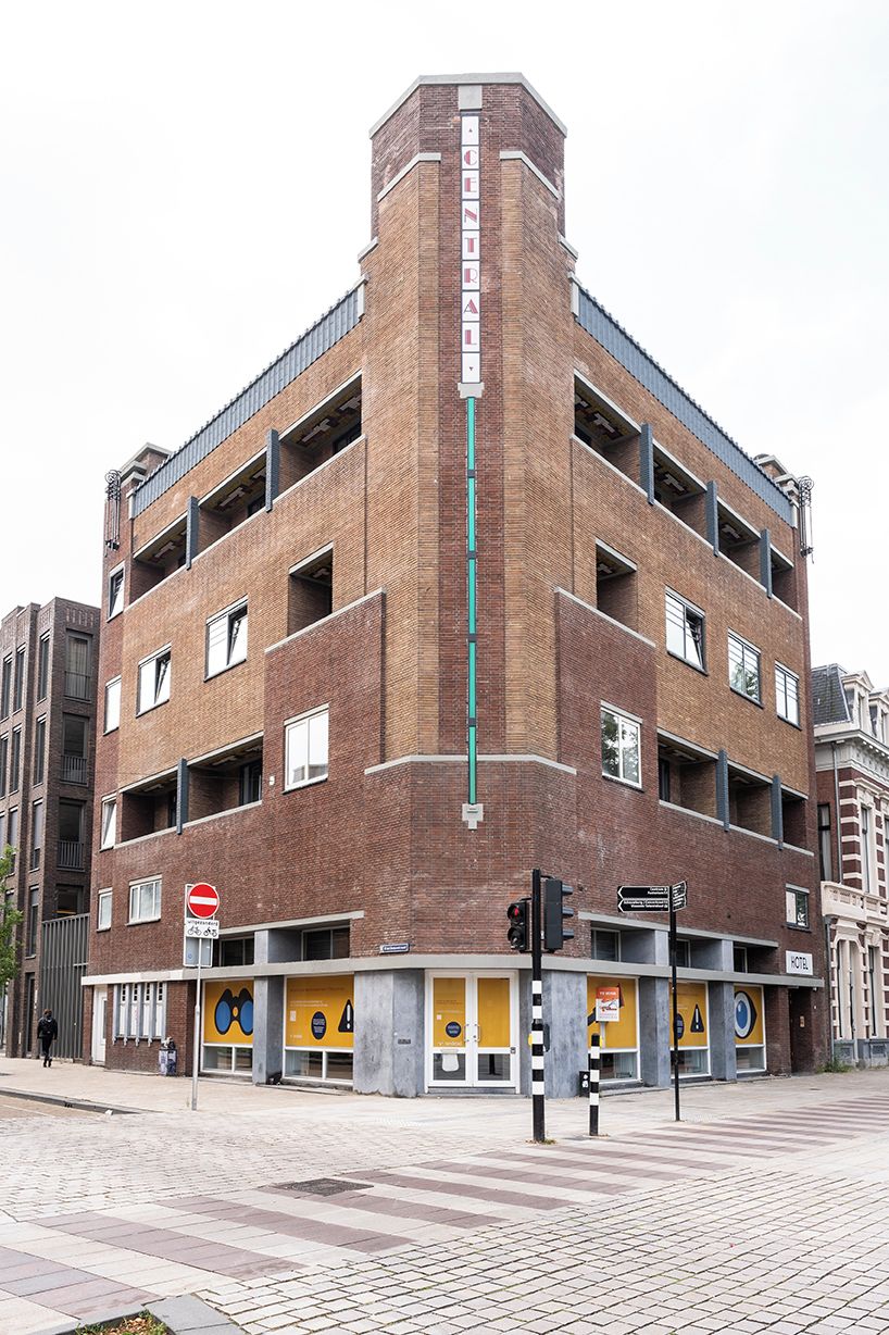 Un edificio a più piani caratterizzato da un elemento verticale centrale, numerosi balconi e un ingresso a livello strada con un cartello.