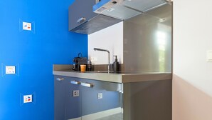 A modern kitchen with a blue accent wall, stainless steel appliances, and a window providing natural light. - Unique apartment with private kitchen and bathroom inspired by the art of Bart van der Leck. (Tilburg)