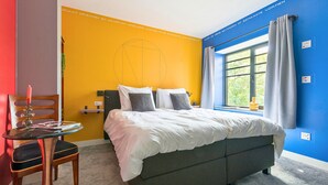 A modern bedroom with a bed, a chair, a table, and a window with curtains. - Unique apartment with private kitchen and bathroom inspired by the art of Bart van der Leck. (Tilburg)