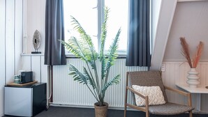 A room with a potted fern, a wicker chair with a cushion, a small table with a laptop and a mug, and a radiator.