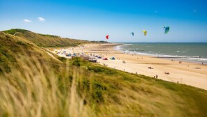 Une plage avec des dunes, une étendue de sable et quelques personnes.