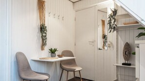 Une petite cuisine moderne avec des meubles blancs, deux chaises grises, une petite table et des plantes décoratives.