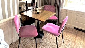 A dining area with a wooden table, pink upholstered chairs, and a window with curtains.