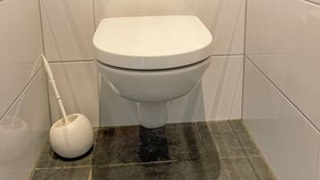Een wit toilet met een spoelhendel, een zuiger en een bedieningsknop aan de muur.