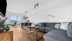 Ett modernt vardagsrum med en grå soffa, ett träbord och en matplats med stolar och ett bord.