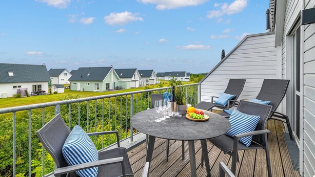 En terrass med utomhusmöbler, ett bord med en fruktskål och glas, och en utsikt över hus i bakgrunden.