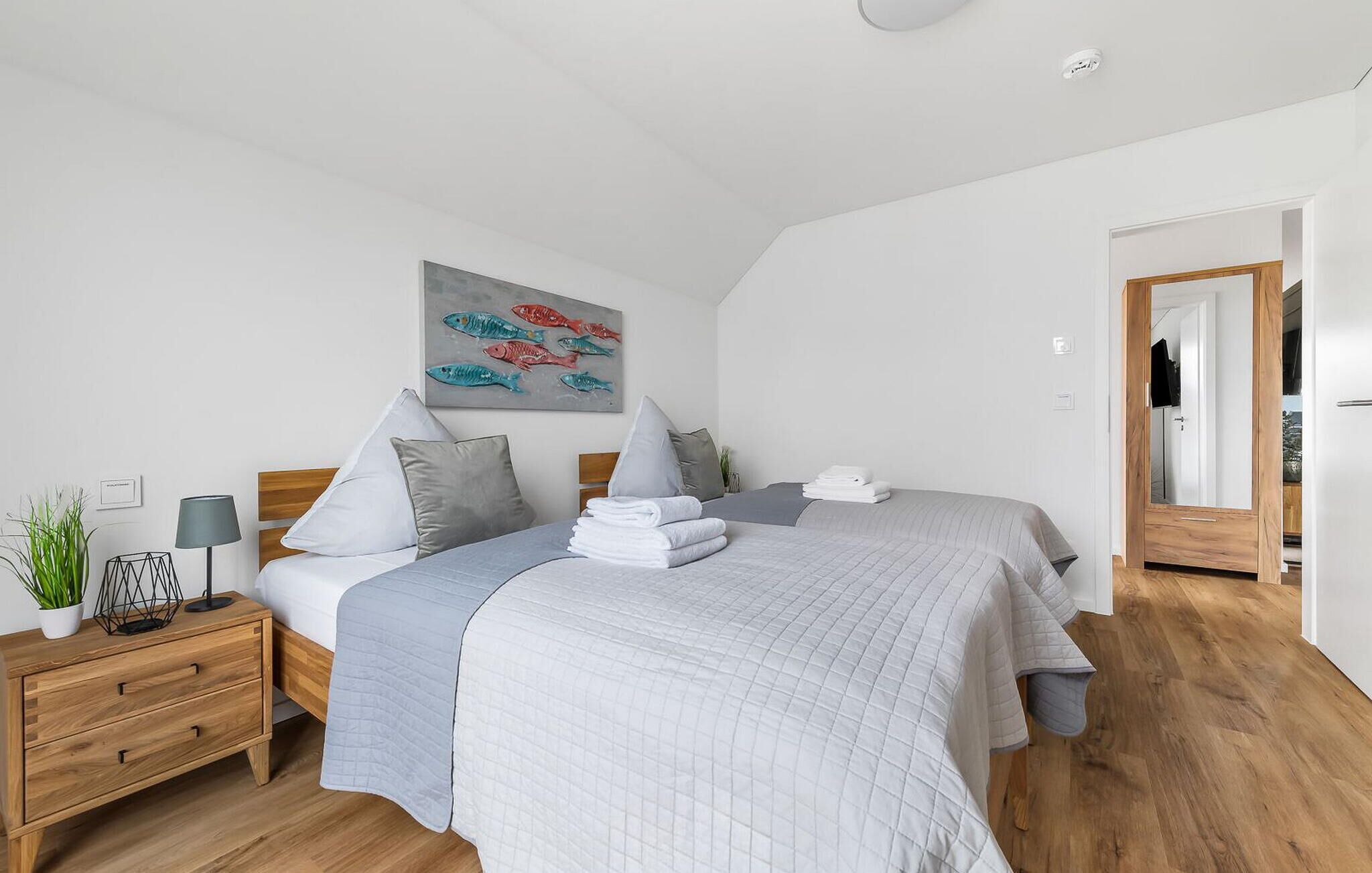 Une chambre à coucher moderne avec un grand lit, deux tables de chevet, une commode, une lampe fixée au mur et un tableau.