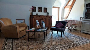 Un salon chaleureux avec un fauteuil en cuir marron, un fauteuil foncé agrémenté d’un coussin, une table basse avec des magazines, un tapis à motifs et un meuble en bois avec un miroir.