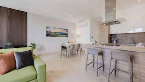 Una cocina moderna con una isla central, un comedor con mesa y sillas, y un sofá verde con cojines.