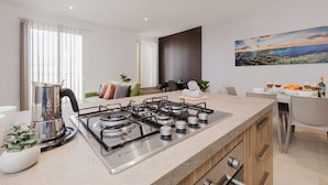 Una cocina moderna con estufa a gas, cafetera y comedor con una mesa lista para dos.