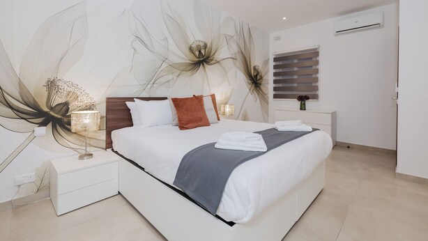 Un dormitorio moderno con una cama grande, una mesita de noche con lámpara y un aire acondicionado de pared.