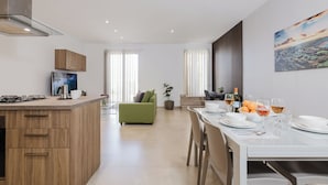 Una cocina moderna con armarios de madera, un comedor con mesa y sillas blancas y un sofá verde al fondo.