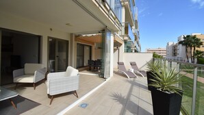 A modern outdoor balcony with wicker furniture, a glass door leading inside, and a view of the cityscape.