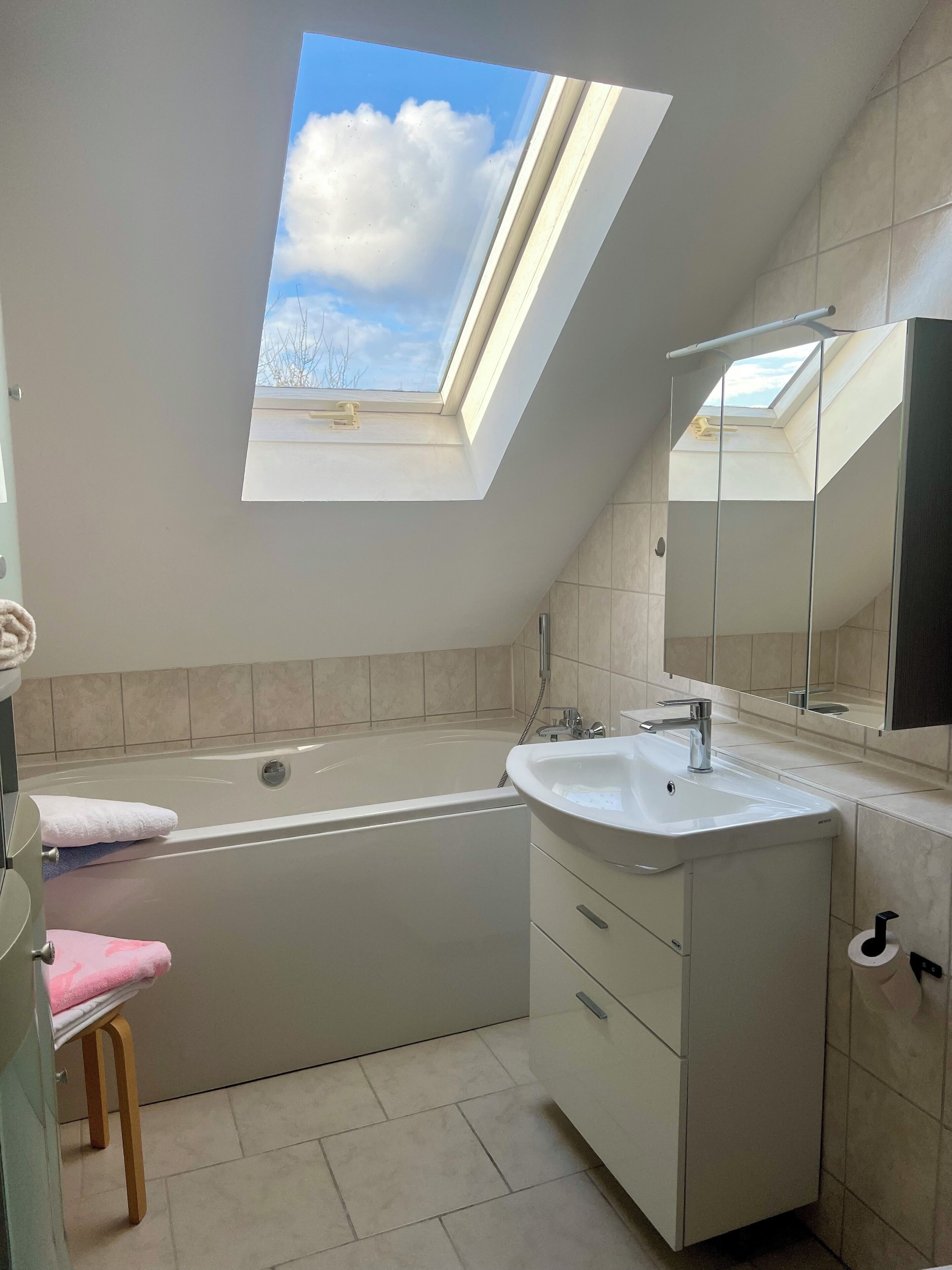 Een moderne badkamer met dakraam, bad, wastafel en badkamermeubel.