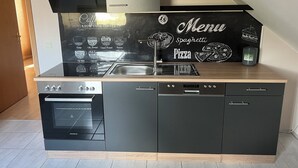 A modern kitchen with a black backsplash featuring a menu of coffee and pizza options. - Ferienwohnung im Grünen (Hainichen)