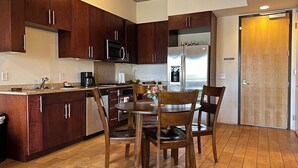 Une cuisine moderne avec des meubles en bois foncé, des appareils électroménagers en acier inoxydable et un coin repas doté de chaises en bois.