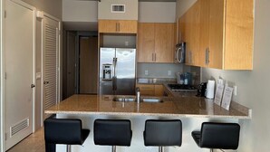 A modern kitchen with a granite countertop, stainless steel appliances, wooden cabinets, and four black bar stools. - Balcony Luxury High Rise Downtown Fremont Casinos (Las Vegas)