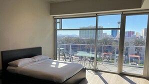 A modern bedroom with a large bed, a balcony with a glass door, and a city view. - Balcony Luxury High Rise Downtown Fremont Casinos (Las Vegas)