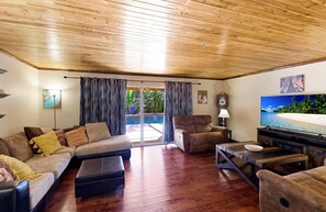 Ein geräumiges Wohnzimmer mit Holzboden, einem großen Flachbildfernseher und einer Glasschiebetür, die zu einem Poolbereich führt.