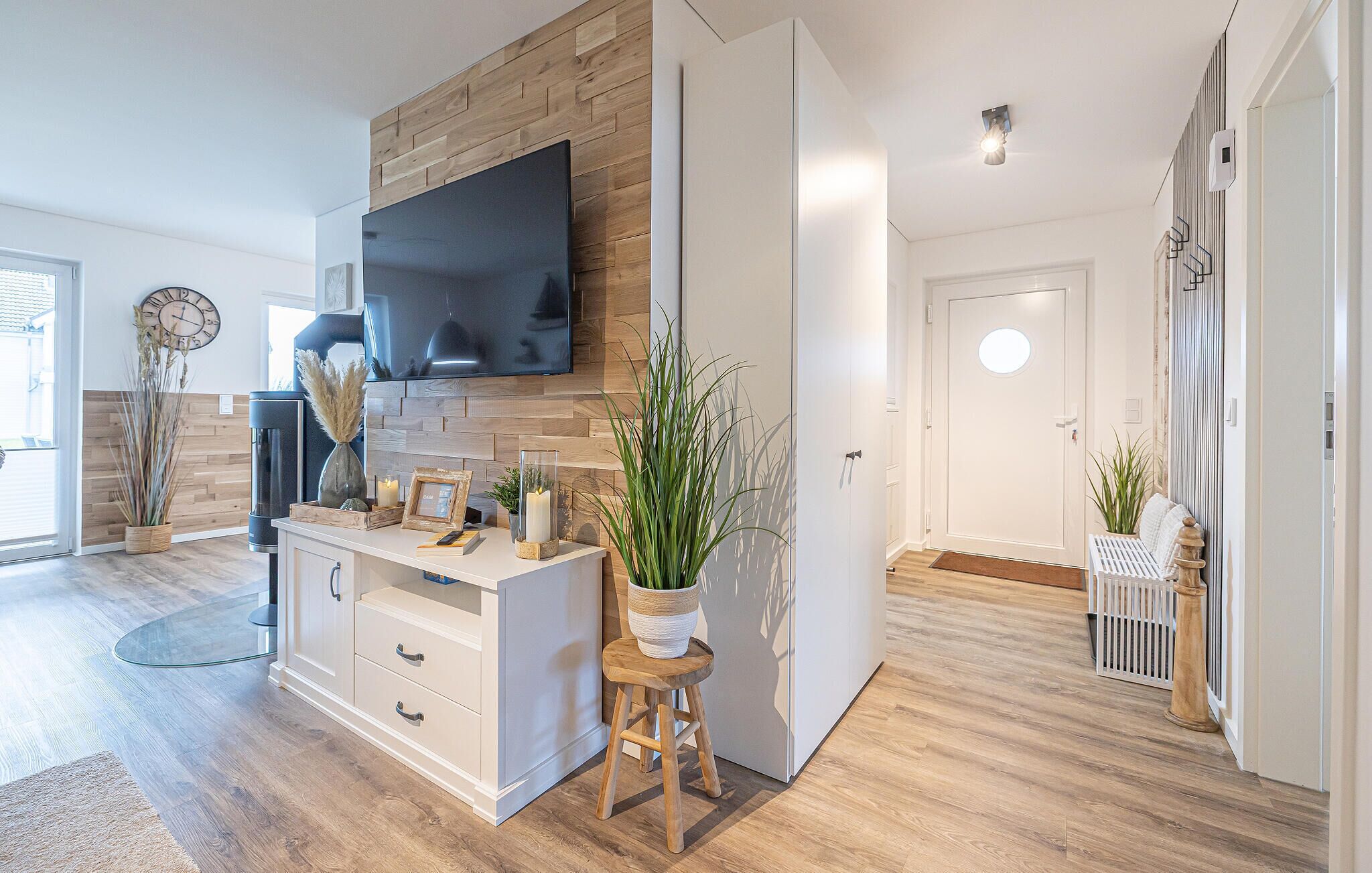 A modern living room with a flat-screen TV, wooden wall paneling, a white console table, and a potted plant.