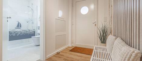 A hallway with a wooden floor, a white bench, a round door, and a bathroom with a sailboat mural.