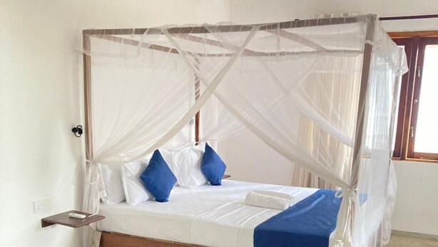 A four-poster canopy bed with a wooden base, white bedding, and blue pillows. - Mealanies House (Unawatuna)