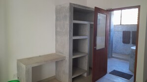 A room with a built-in wardrobe, a small bench, a green basket, and a door leading to a bathroom with a towel rack. - Mealanies House (Unawatuna)